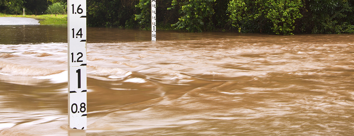 Brown flood water over a road with flood depth indicators