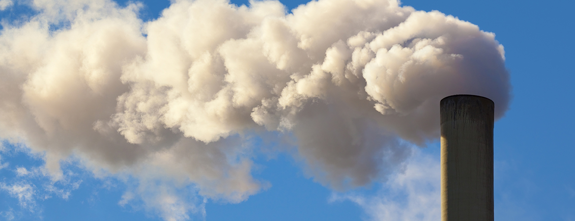 Clouds billowing from a factory smokestack against a blue sky background